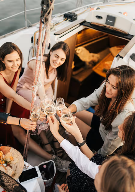 Group of young women sitting on a boat, clinking wine glasses in a celebratory toast.