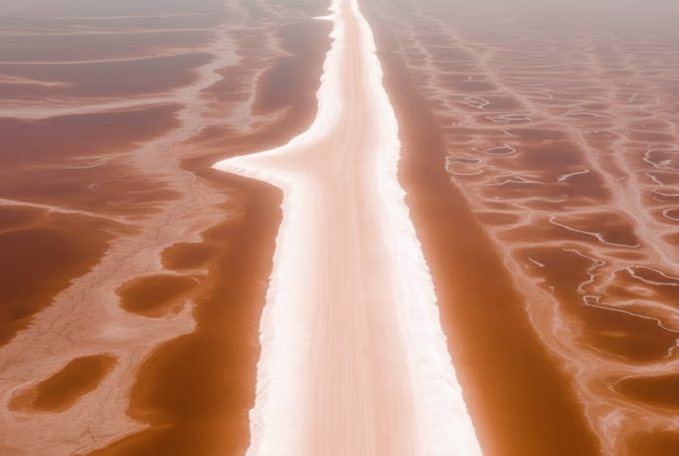 Aerial view of a narrow white salt road cutting through reddish salt flats.