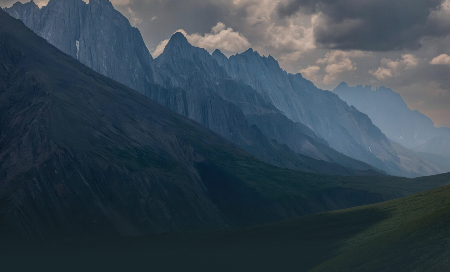 Layered mountain ridges under a cloudy sky with mist in the valleys.
