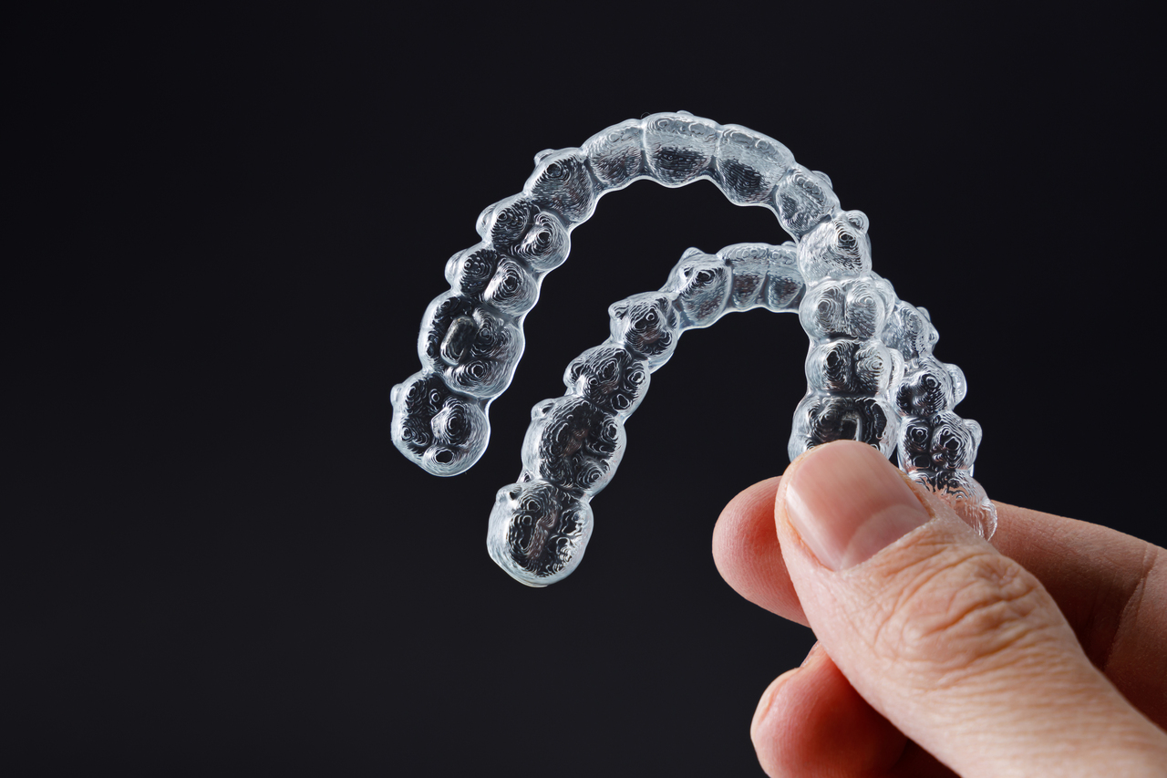 fingers holding up two sets of clear aligners