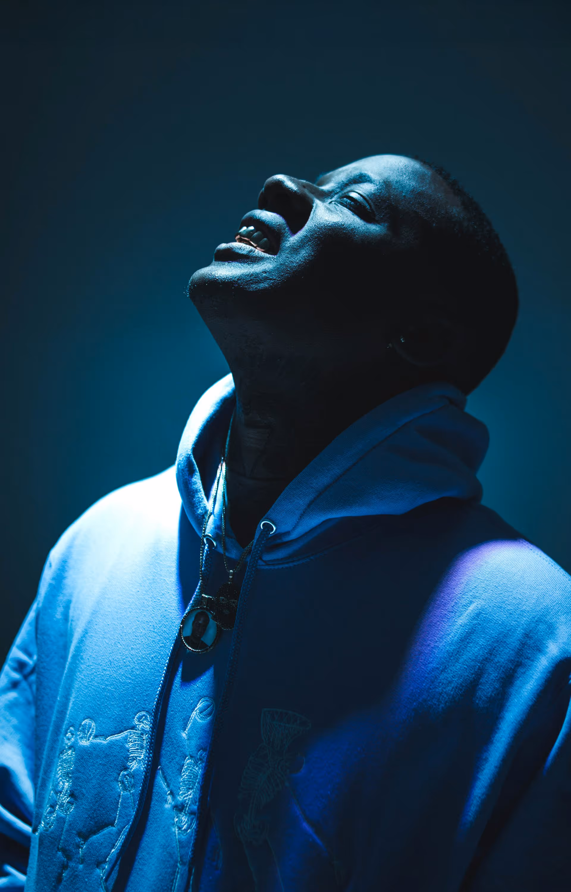 Portrait of a man in a blue hoodie looking upward with a thoughtful expression under dramatic blue lighting.