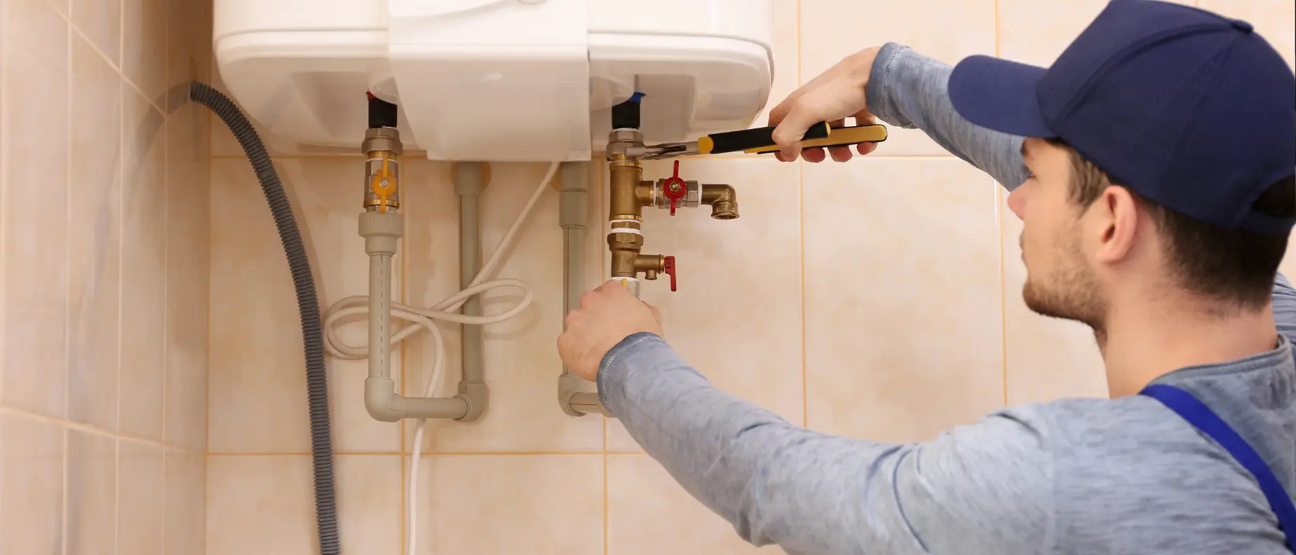 Professional plumber repairing sink drain pipes and tightening fittings under a bathroom sink in a residential home