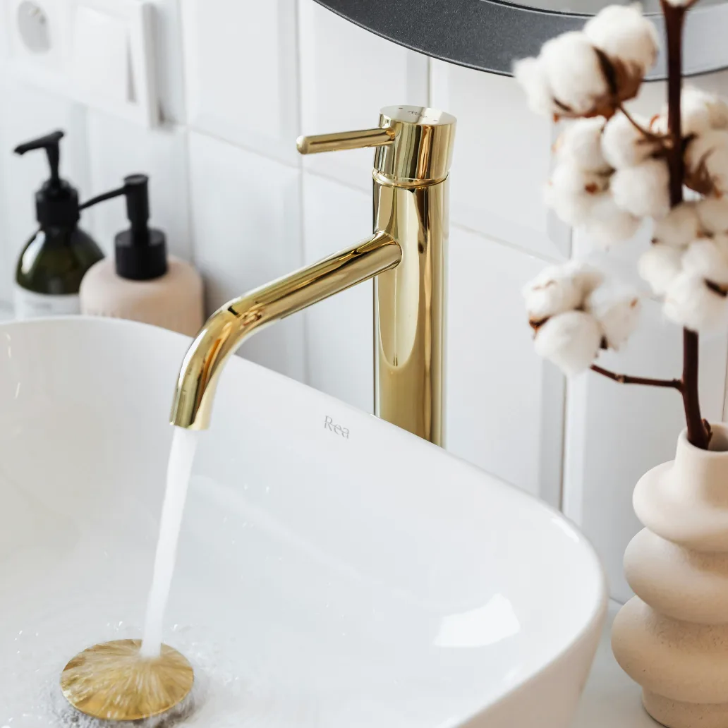 Modern bathroom sink with a gold faucet running water, showing clean water flow and proper plumbing installation.