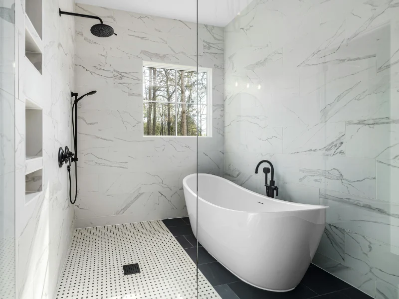 Modern bathroom with a walk-in shower, freestanding tub, and black plumbing fixtures installed against marble tile walls
