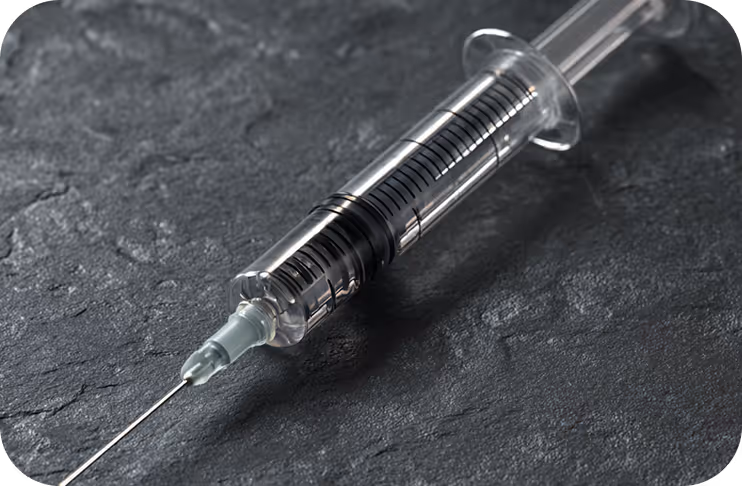 Close-up of a transparent syringe with measurement markings on a dark textured surface.