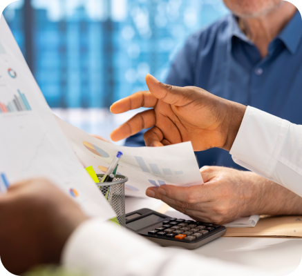 شخصان يحللان تقارير مالية تحتوي على مخططات ورسوم بيانية، مع وجود آلة حاسبة على المكتب.