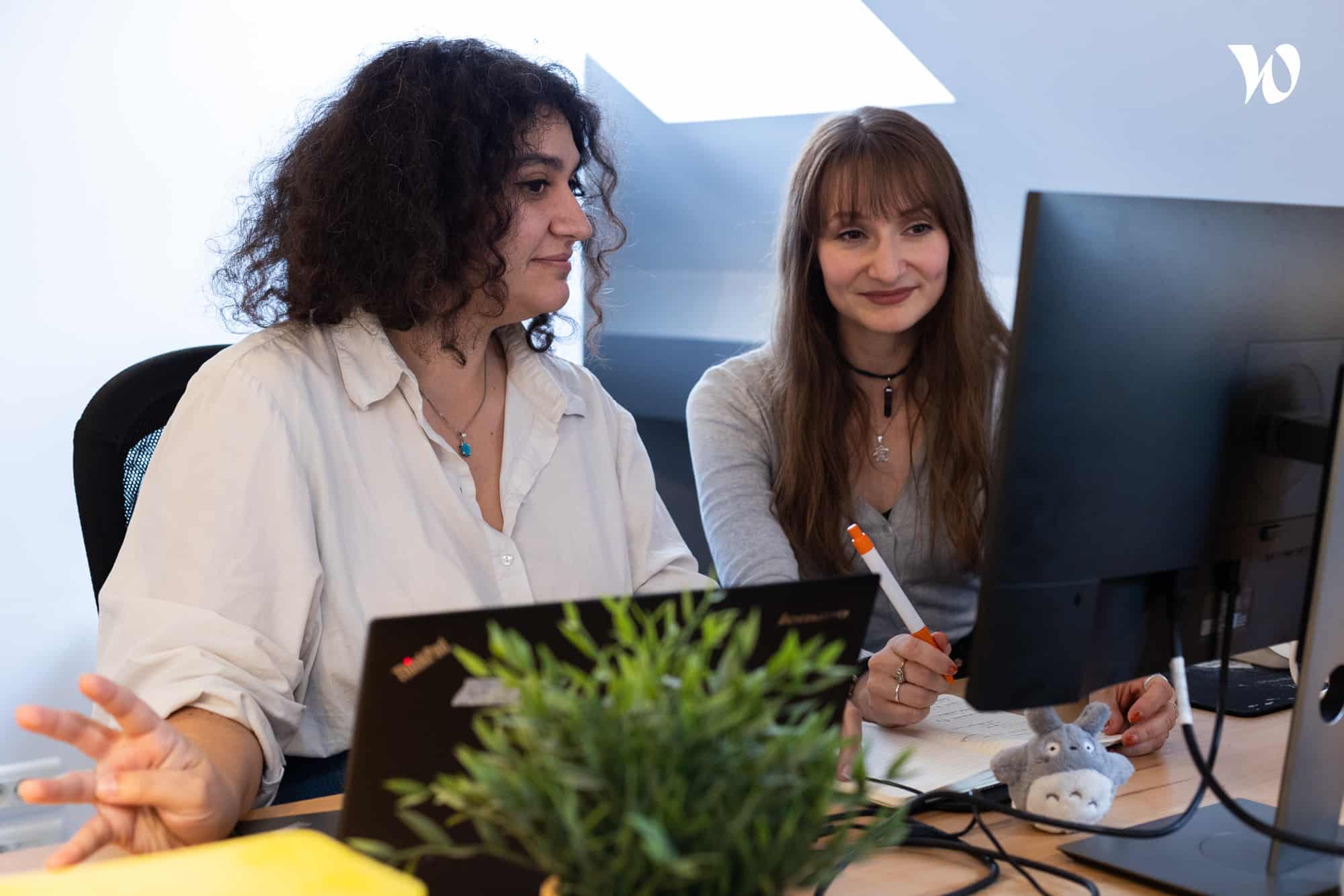 Deux femmes travaillant ensemble sur des ordinateurs dans un bureau moderne avec une plante sur le bureau.