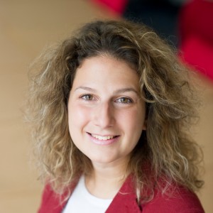Portrait en gros plan d'une femme souriante aux cheveux bouclés et portant un pull rouge.