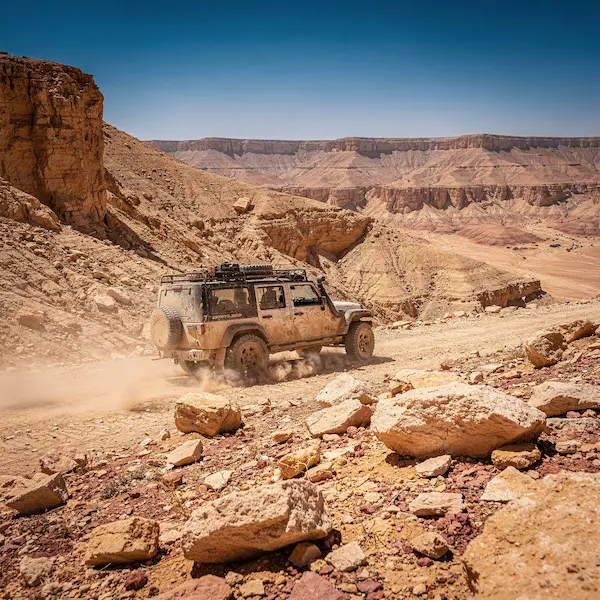 ג'יפ טיולים נוסע בתוך מכתש רמון על רקע קירות המכתש הצבעוניים
