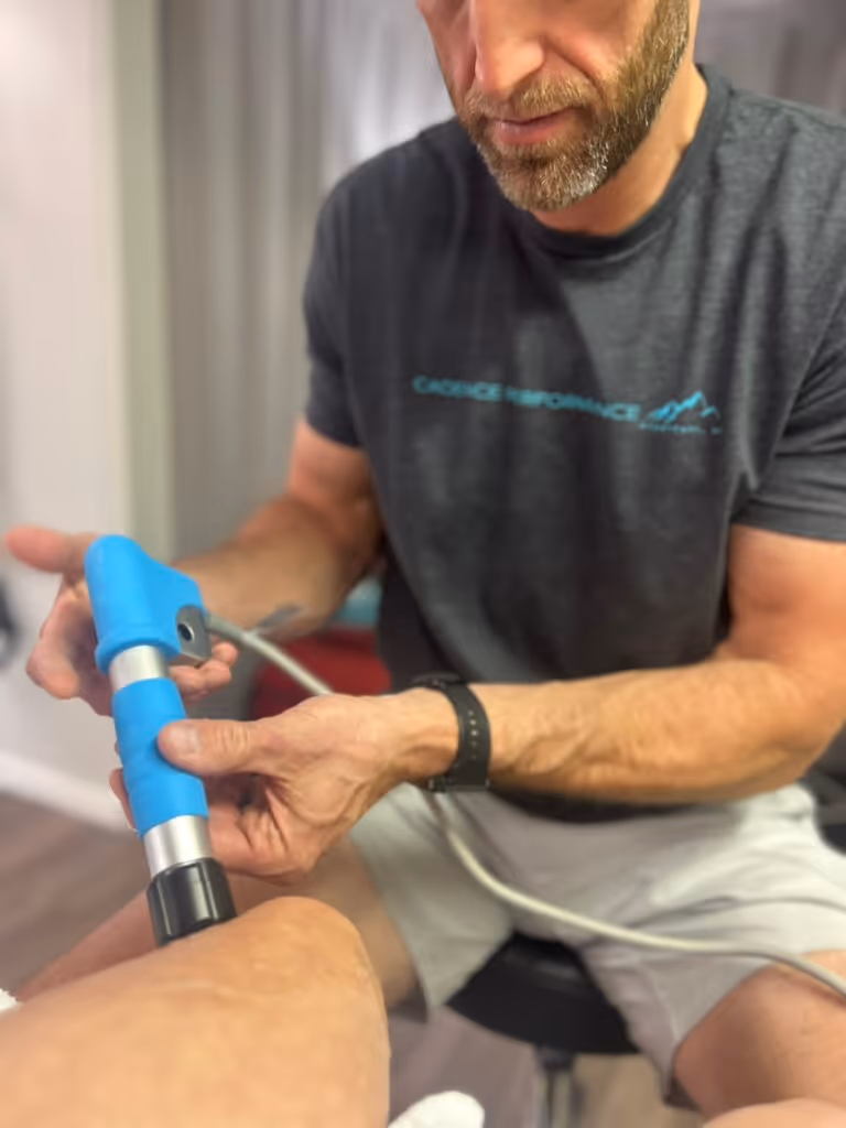 Man using a blue handheld therapy device on a person's knee in a clinical setting.