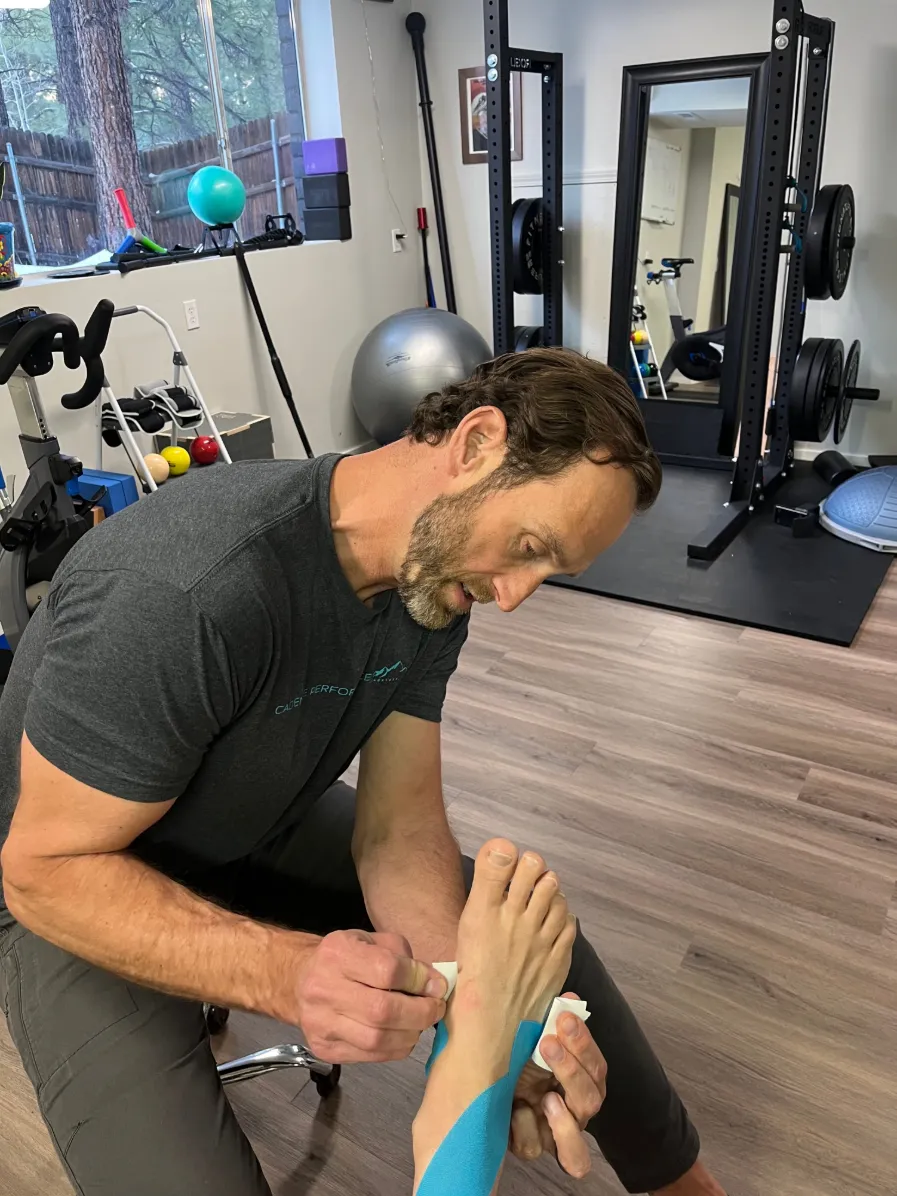 Man applying blue kinesiology tape to a person's foot in a home gym setting.