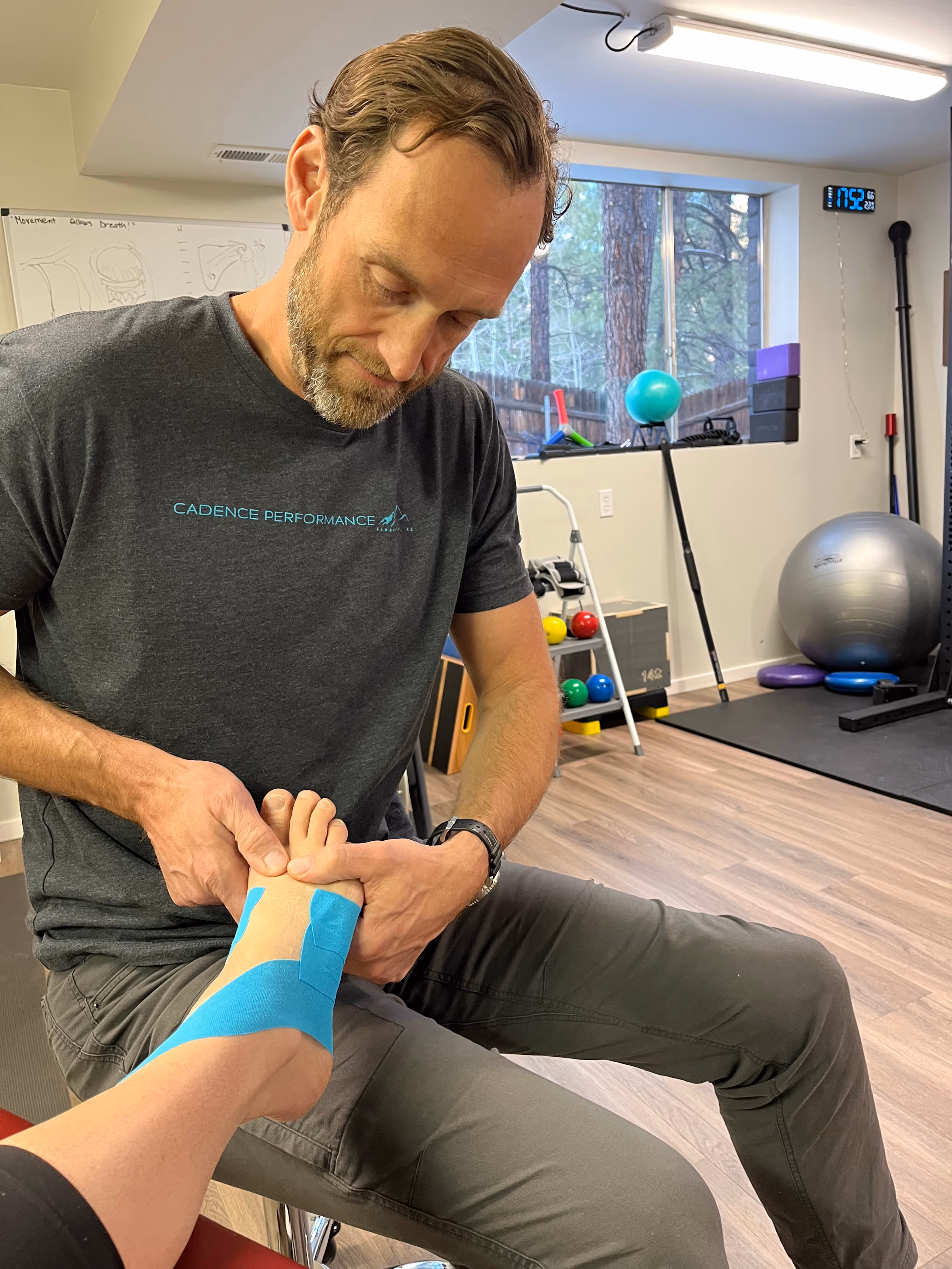Therapist applying blue kinesiology tape to a person's ankle in a fitness therapy room.