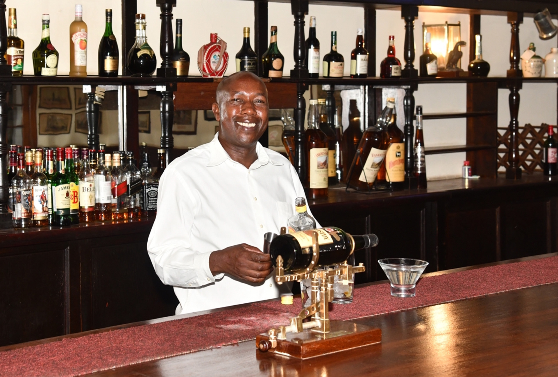 Barmann Neyasha schenkt Drinks an der Holztheke des historischen Bulawayo Club Hotel aus – einst Gentlemen’s Club, heute Ort für Begegnungen.