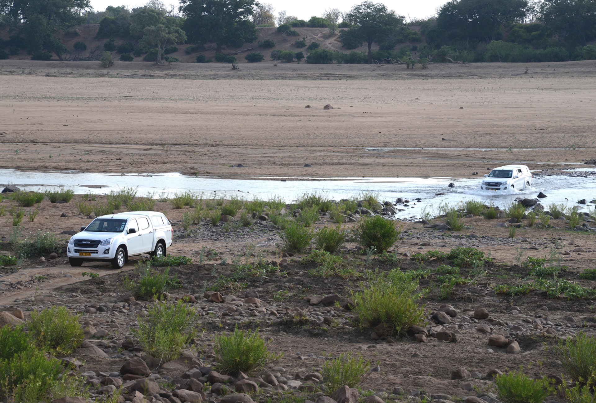 Geländefahrzeuge durchqueren den Runde River im Gonarezhou Nationalpark und kehren von der Safari zu Zeltcamps mit Blick auf Wildtiere zurück.