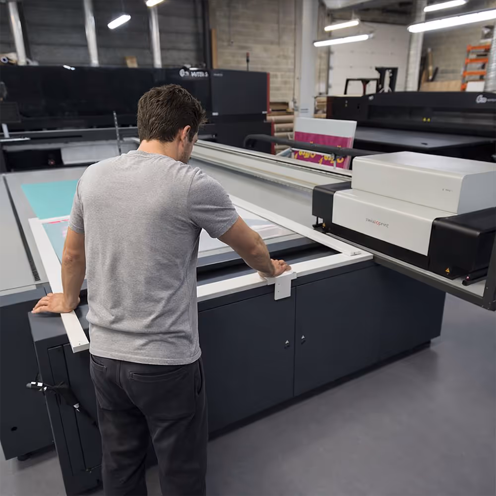 Man operating a large flatbed printer in a commercial printing workshop.