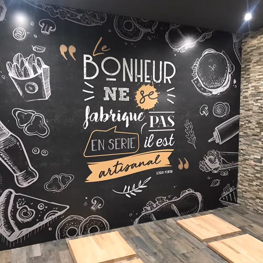 Restaurant wall art with French quote about happiness and artisanal craftsmanship surrounded by white food illustrations on blackboard background.