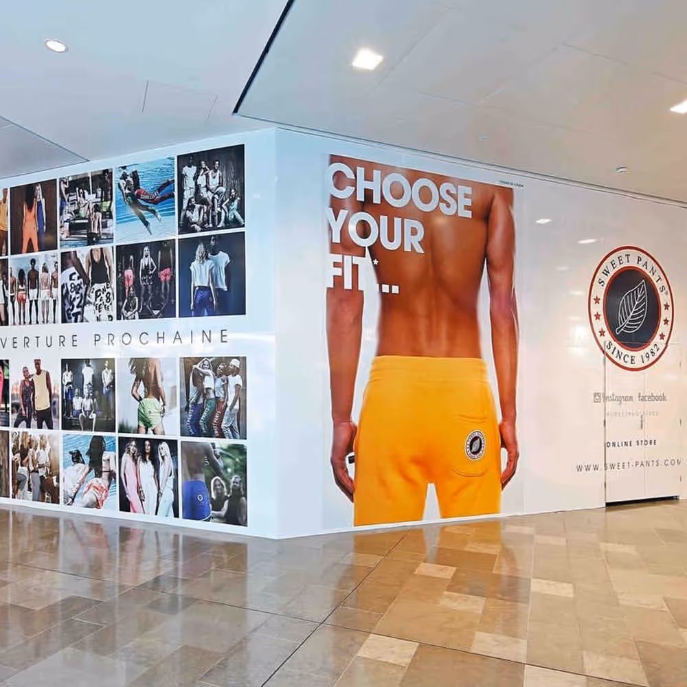 Storefront wall with a large advertisement showing a shirtless person wearing yellow shorts and text 'CHOOSE YOUR FIT...' along with a collage of fashion photos and Sweet Pants brand logo.