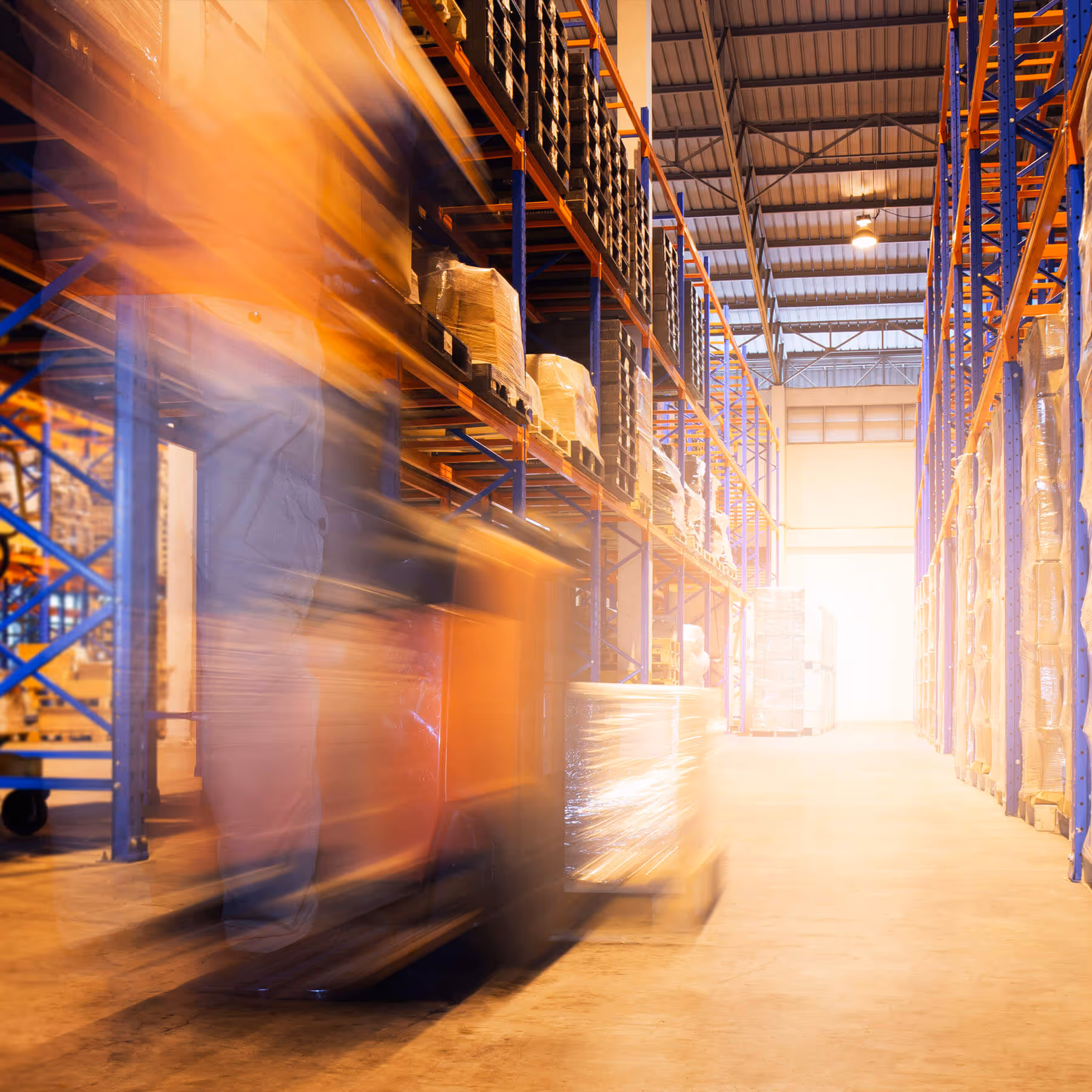 Blurred motion of a forklift carrying wrapped pallets inside a large, organized warehouse with tall shelves.