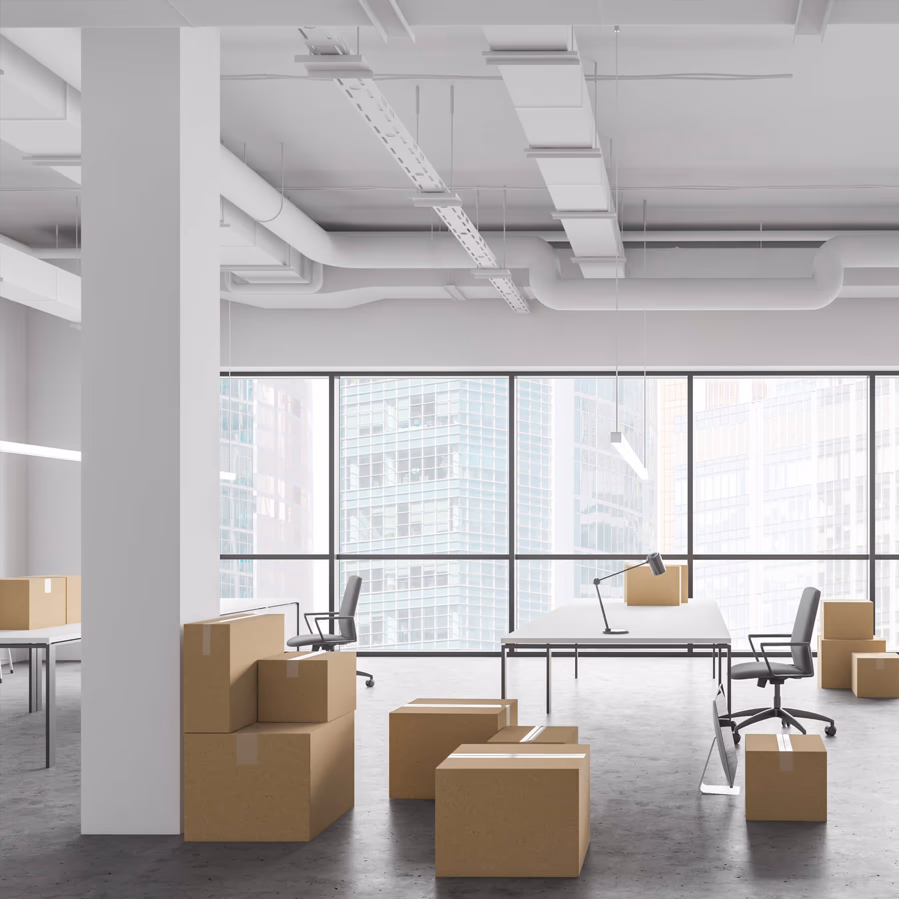 Bright modern office with large windows, empty desks, chairs, and stacked cardboard moving boxes.