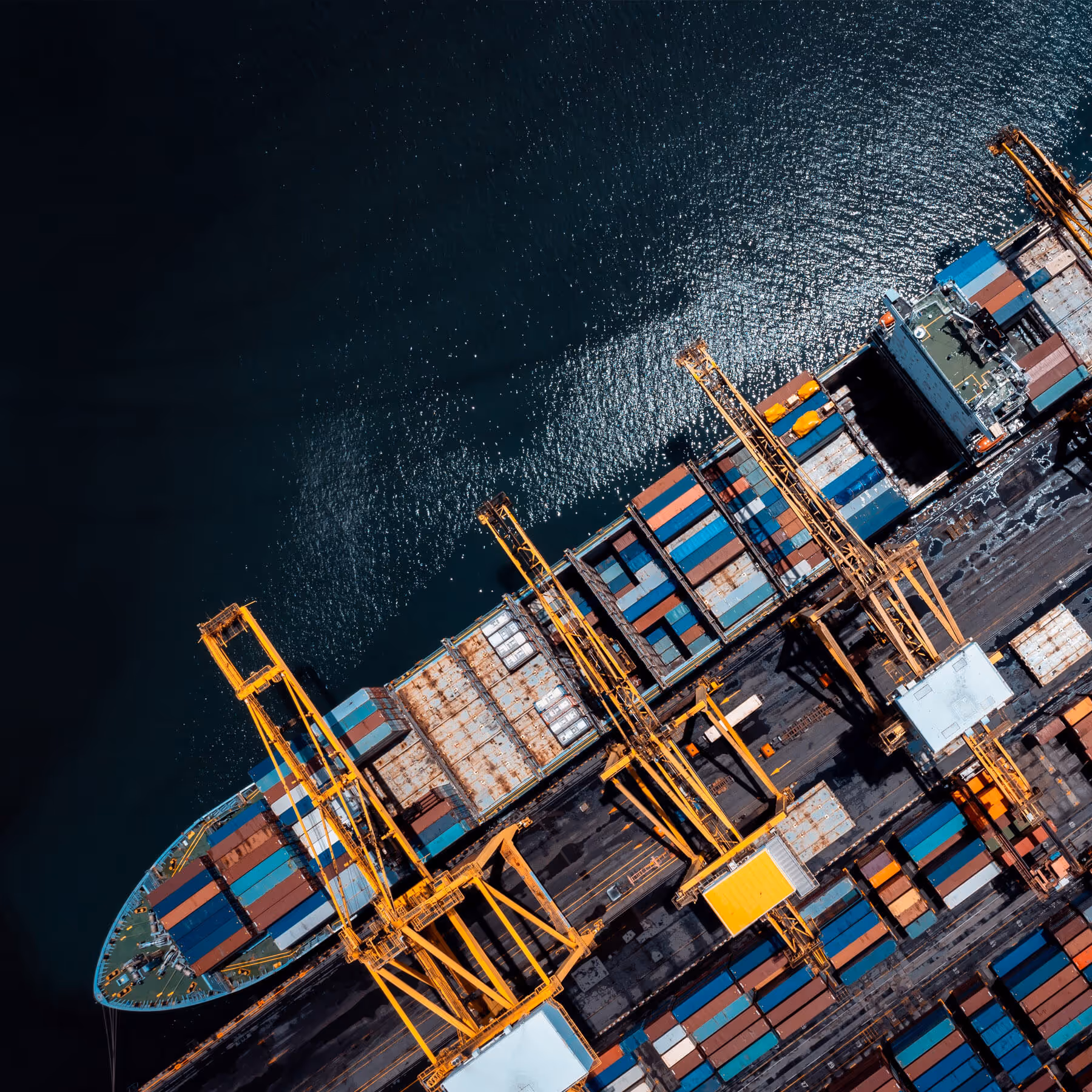 Aerial view of a cargo ship docked at a port with colorful shipping containers and yellow loading cranes.