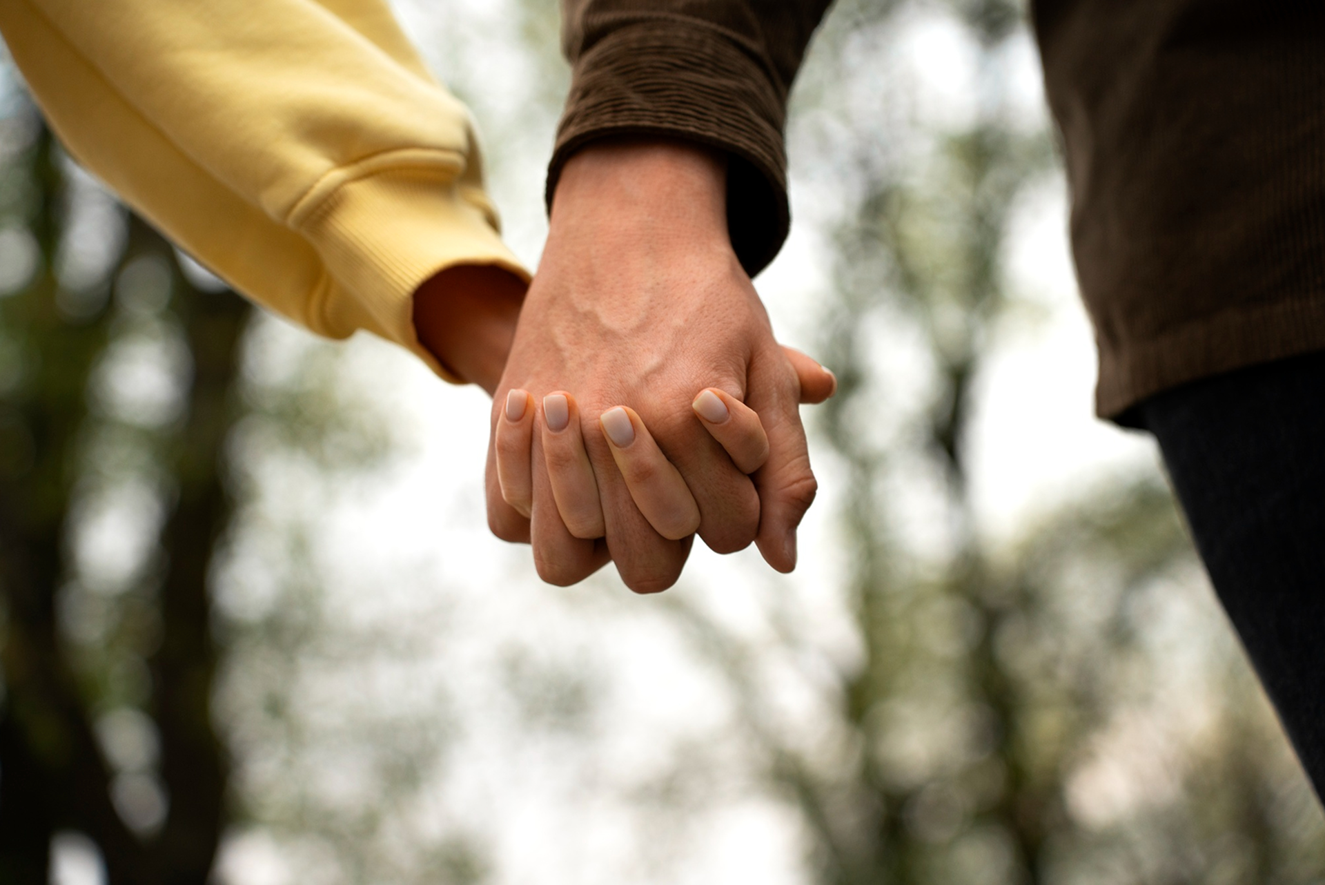 Two people holding hands outdoors with blurred trees in the background.