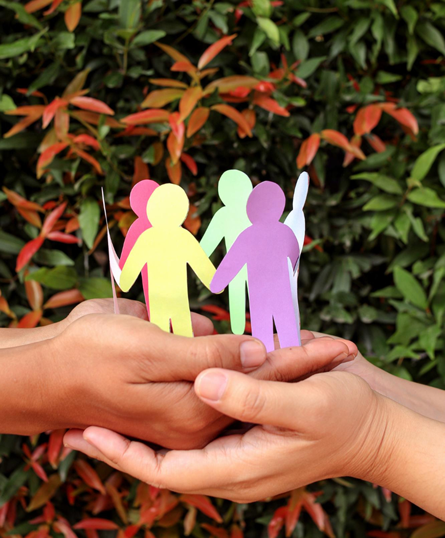 Two pairs of hands holding a circle of colorful paper cutout figures representing unity and support.