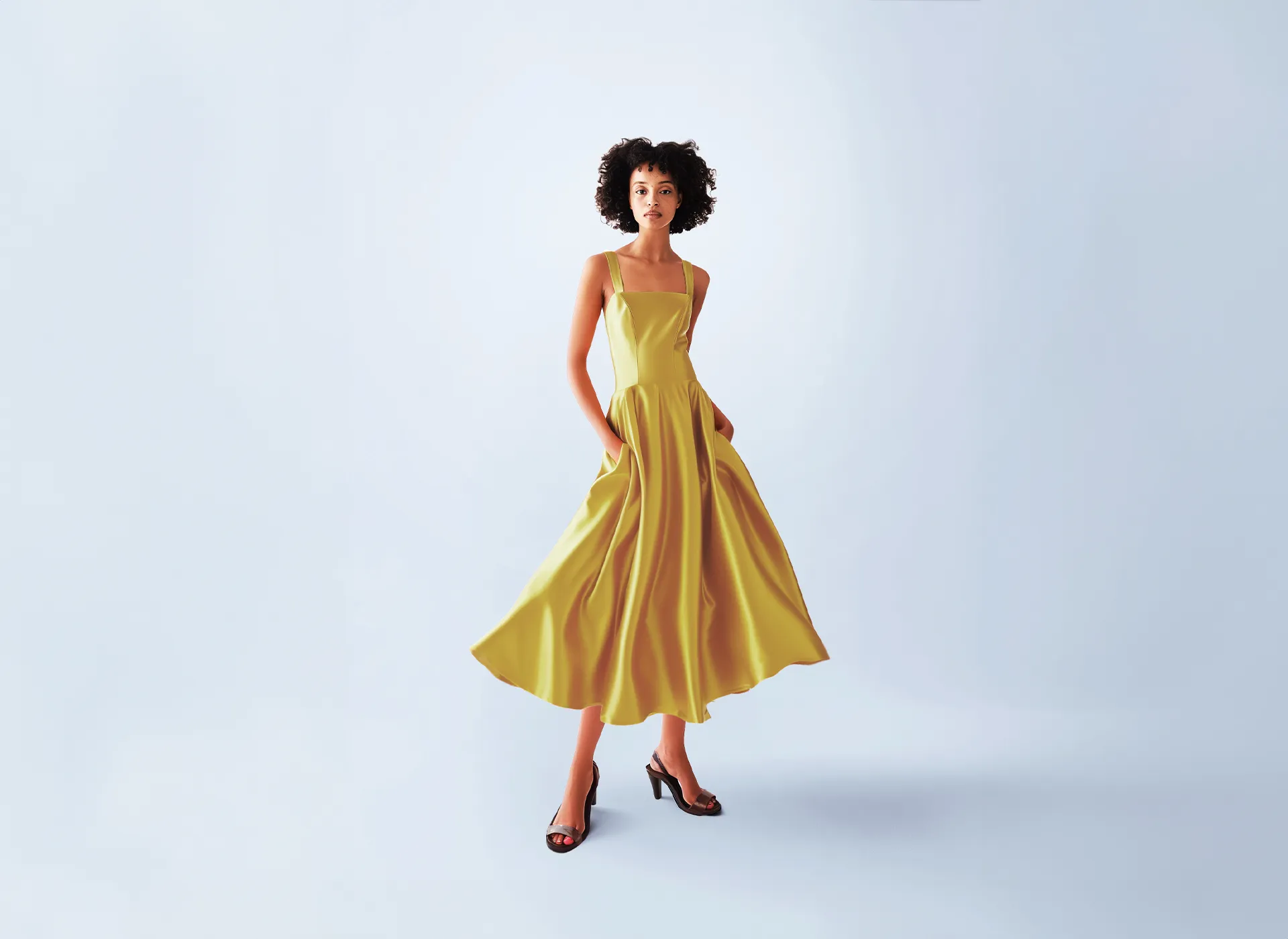 A woman in an orange dress stands in front of a white background.