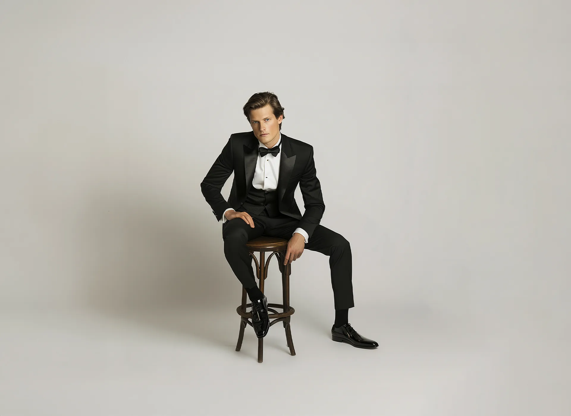 A man wearing a tuxedo and bow tie sitting on a stool.