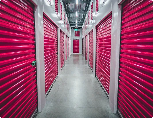 Long corridor in a storage facility with red roll-up doors on both sides and clean concrete floor.
