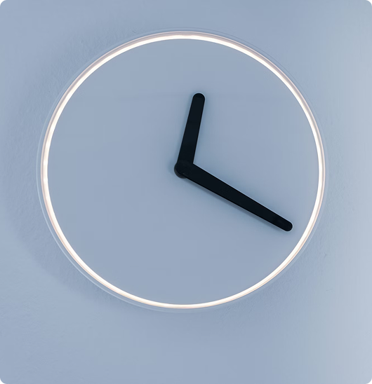 Modern wall clock with illuminated circular frame and black hour and minute hands showing 3:00.