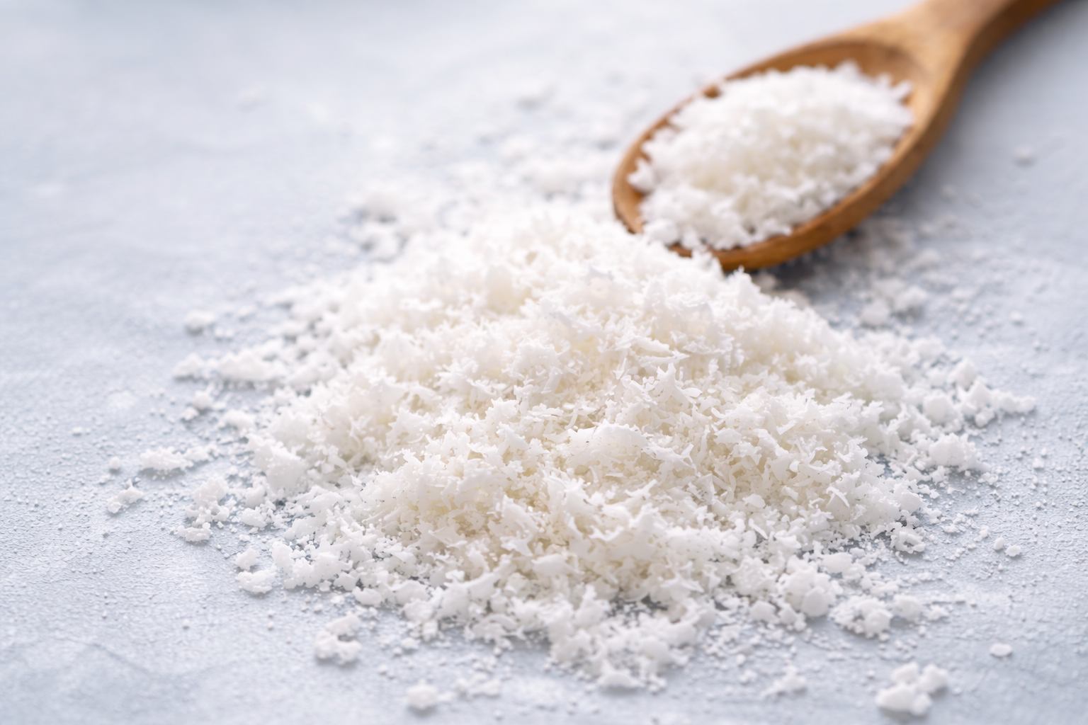 Close-up of finely grated white coconut with some on a wooden spoon.