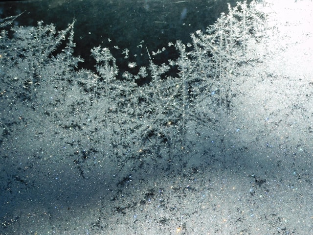 Close-up of intricate ice crystals forming on a frosted window with a dark background.