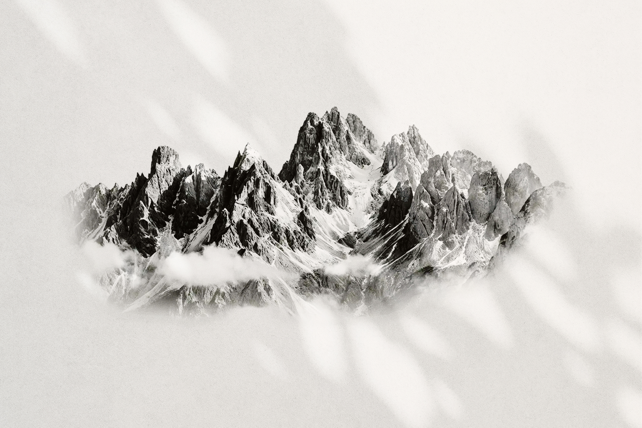 Svart-hvitt bilde av skarpe, snødekte fjelltopper med lave skydekker under.
