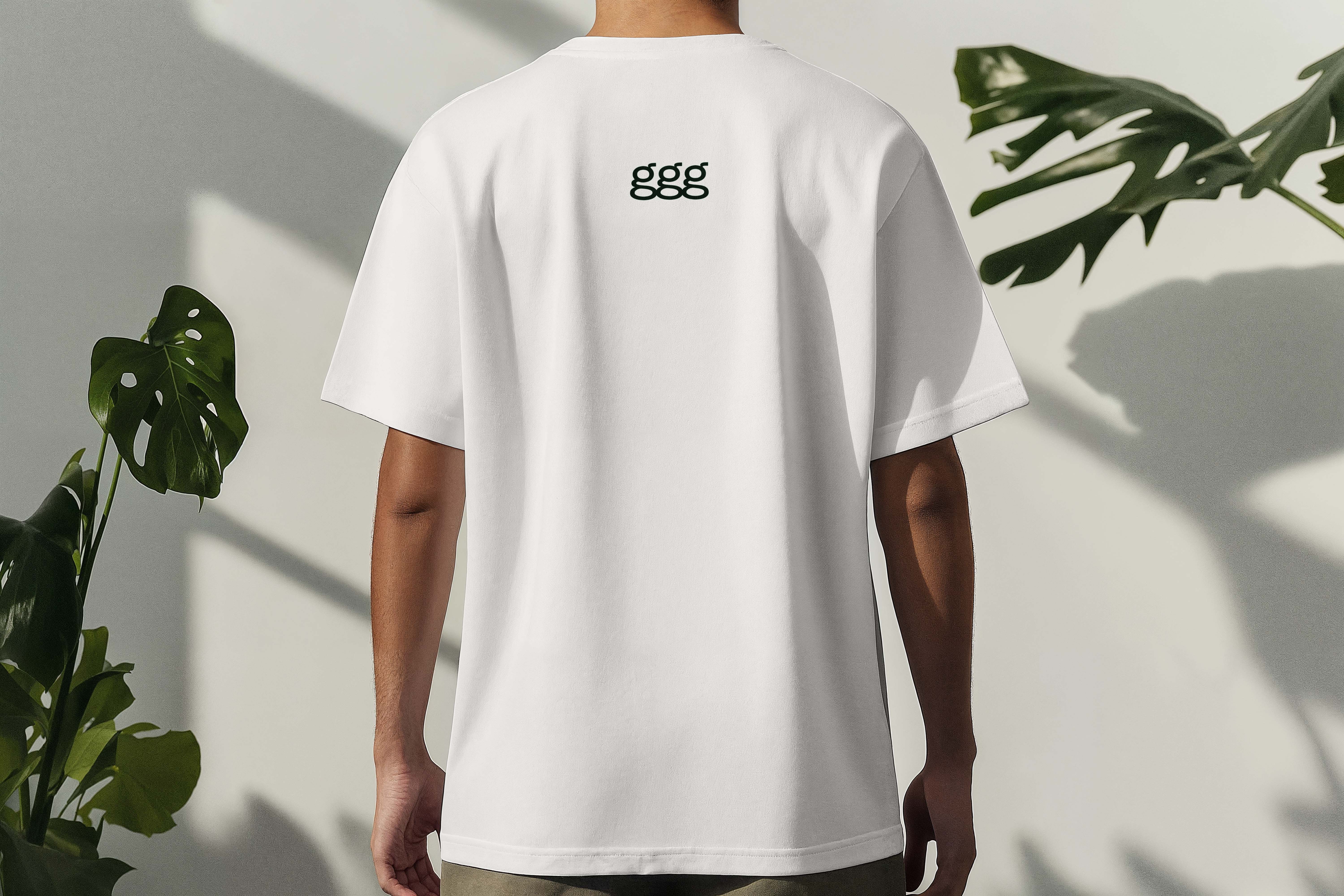 Person sett bakfra iført hvit T-skjorte med svart ggg-logo øverst på ryggen, med grønne planter i bakgrunnen.
