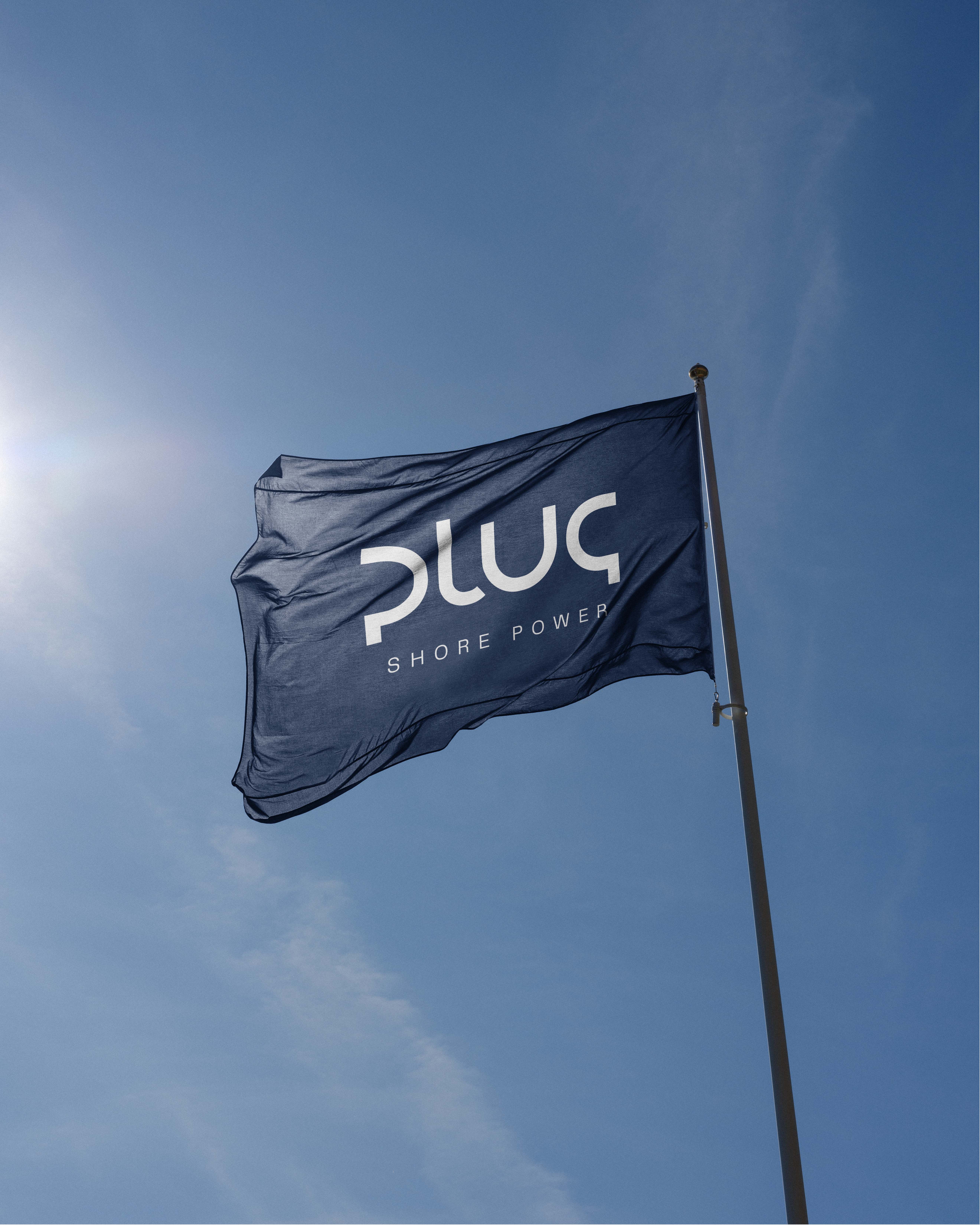 Dark blue flag with white text 'plug SHORE POWER' waving against a clear blue sky with the sun shining.