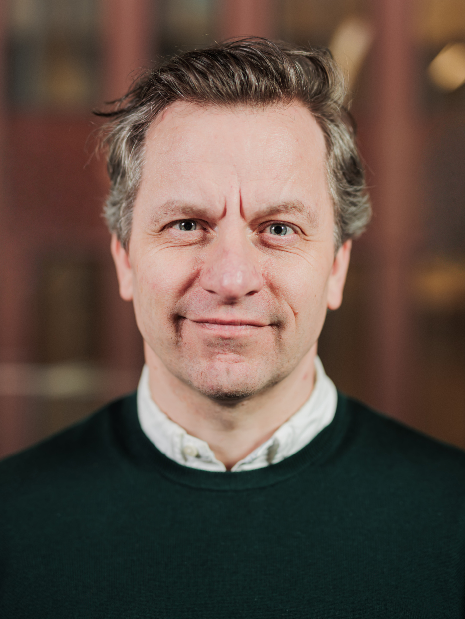 Portrait of a middle-aged man with gray-streaked hair wearing a dark green sweater and white collared shirt.
