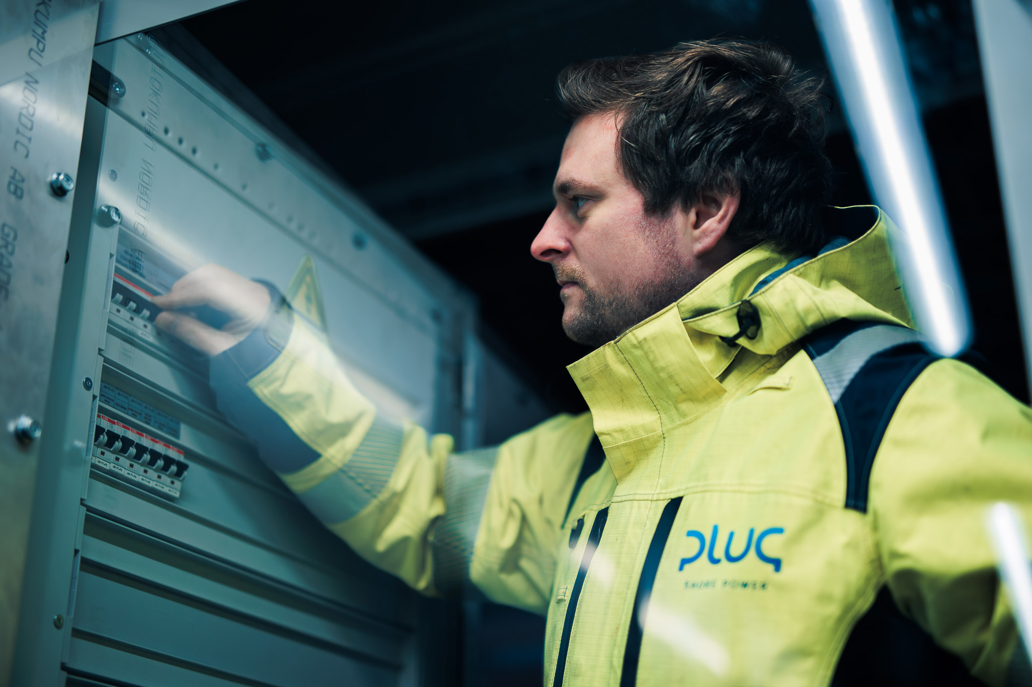 Man in yellow high-visibility jacket adjusting switches inside an electrical control panel.