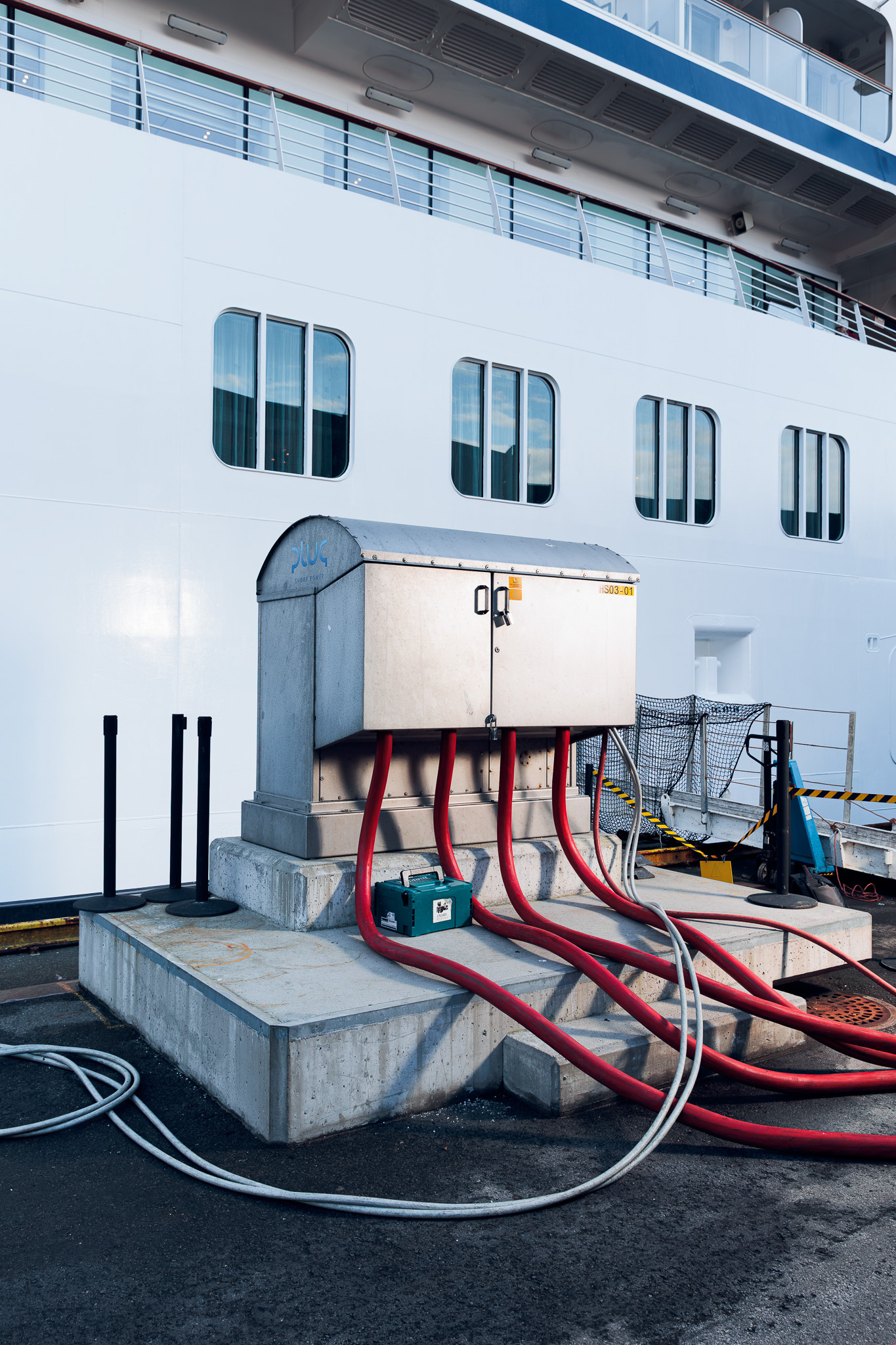 Electrical connection box on a concrete platform with thick red and white cables connected to a docked ship.