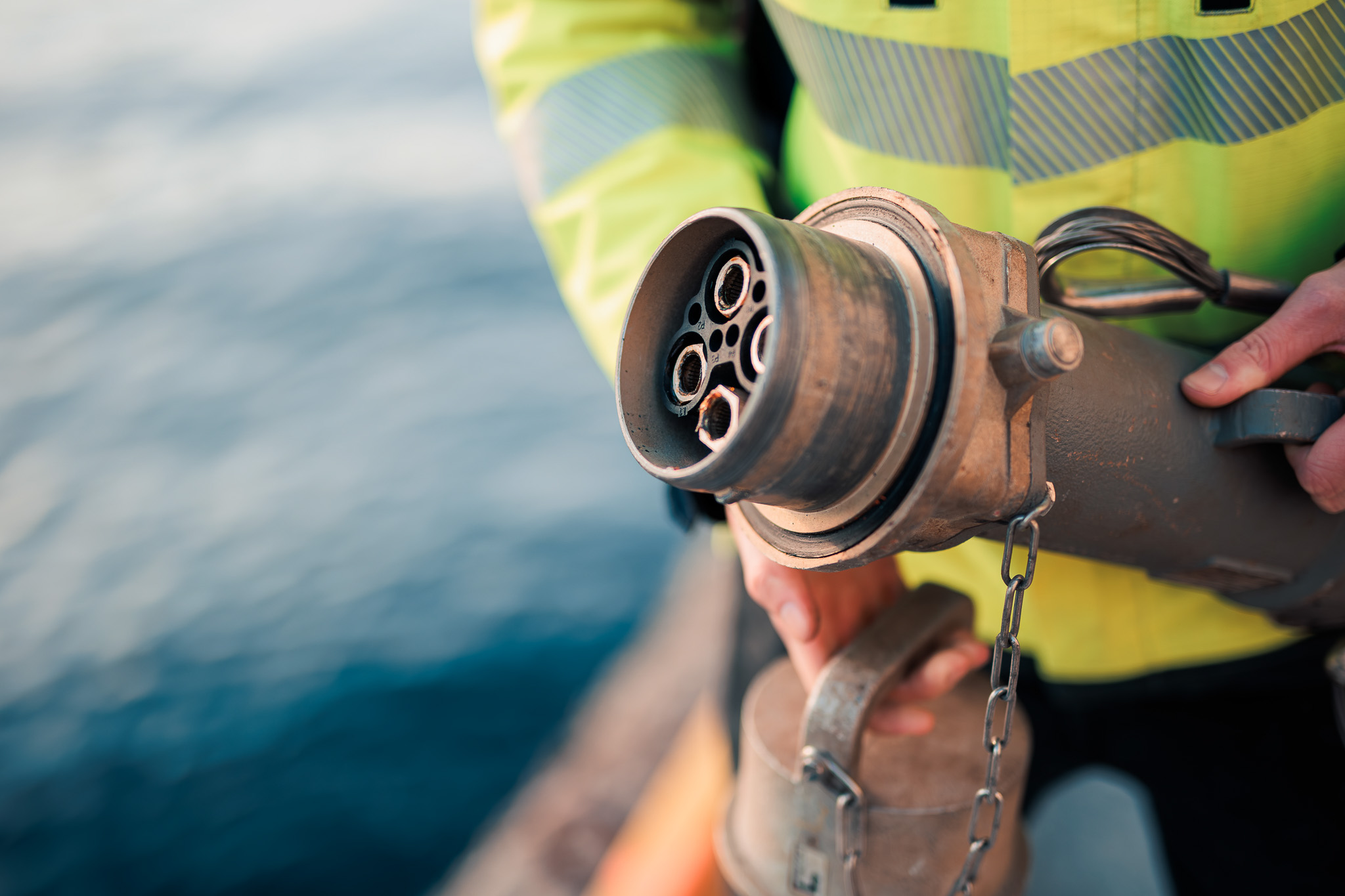 Person holding a large industrial electrical plug near a body of water.