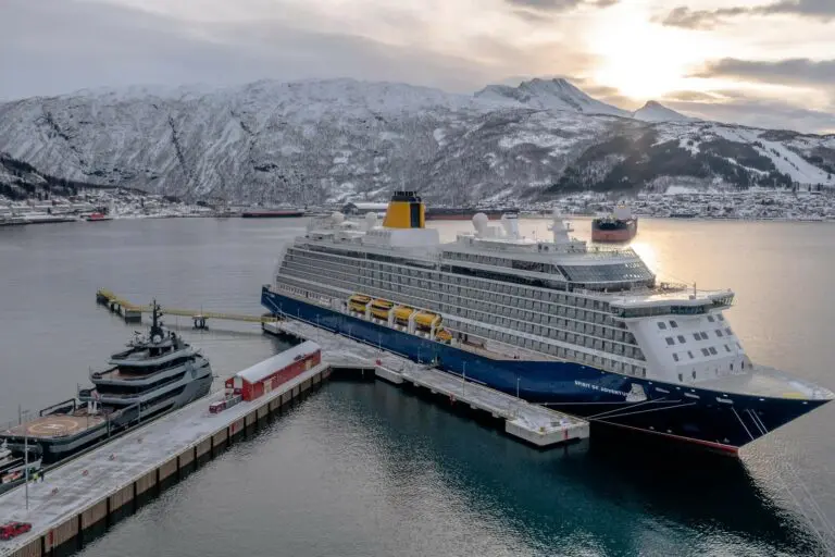 Large cruise ship docked at a snowy harbor with mountains in the background at sunset.
