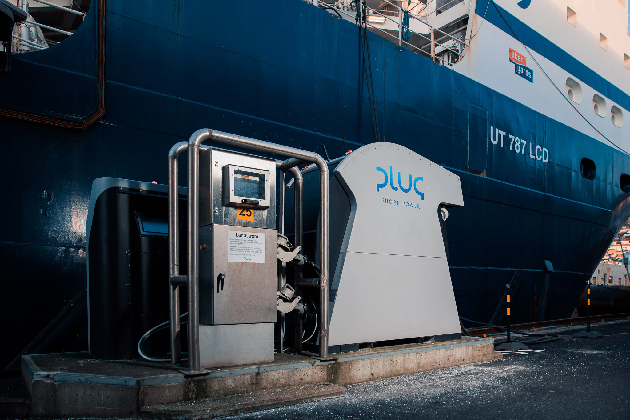 Plug Shore Power electrical charging station on dock next to a large blue and white ship labeled UT 787 LCD.