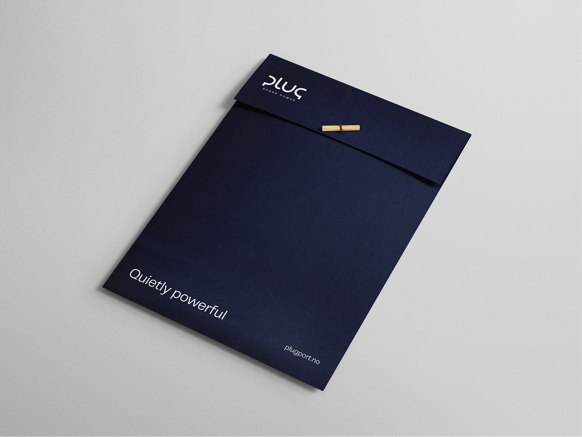 Closed dark blue folder with a wooden button closure, labeled 'plug shore power' and text 'Quietly powerful' with website plugport.no.