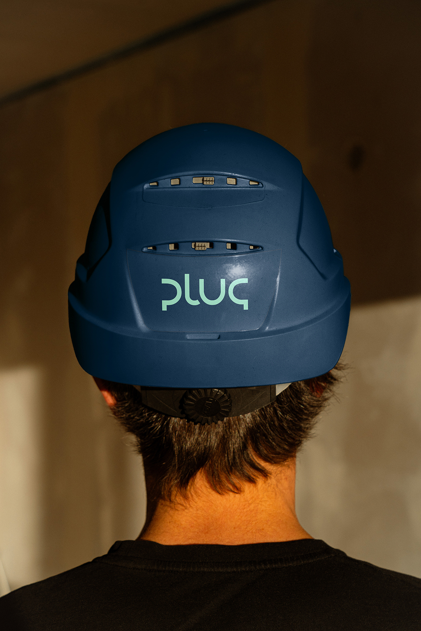 Baksidebilde av en person som bruker en blå hjelm med logoen "plug" i grønt.