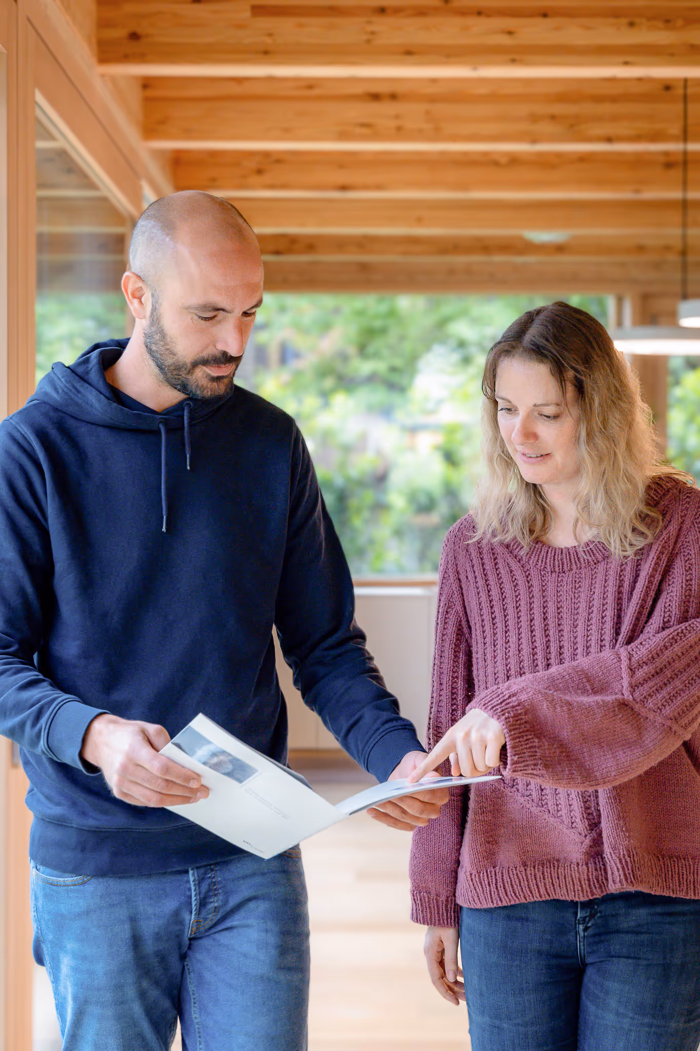 Ein Mann und eine Frau besprechen in einem Holzraum ein aufgeschlagenes Buch oder Magazin, die Frau zeigt auf eine Seite.