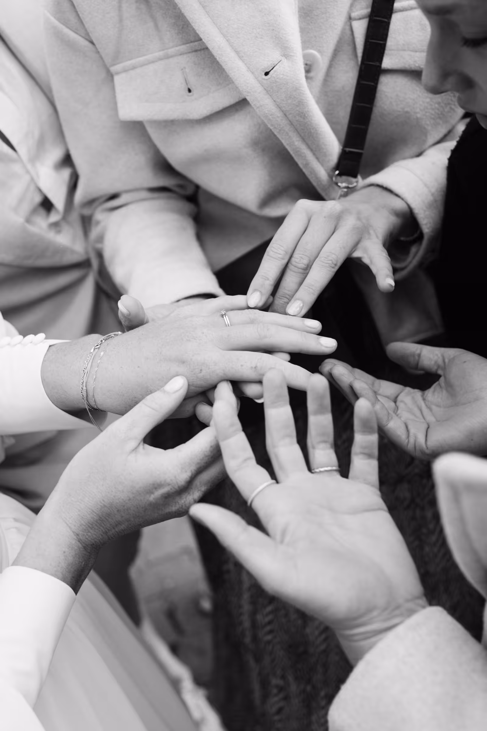 Multiple hands gathered around a hand wearing an engagement ring, showing support and admiration.