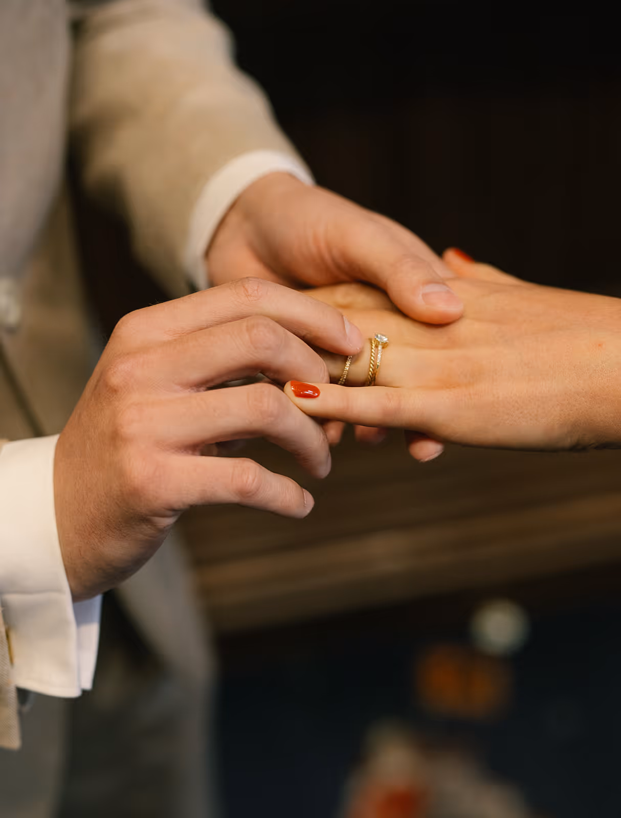 Close-up of a person placing a gold ring with a diamond on another person's finger with red nail polish.
