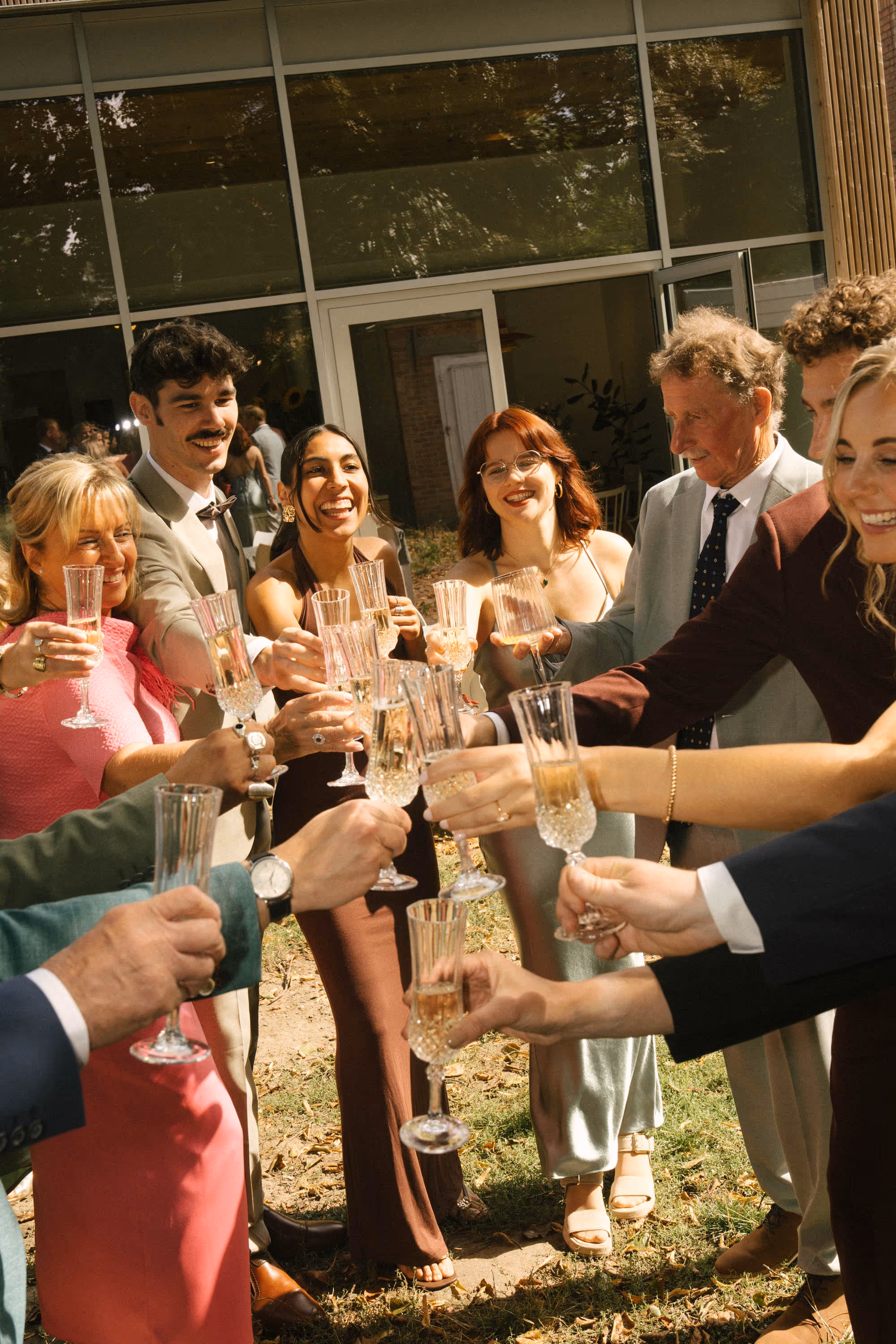 Group of well-dressed people outdoors raising champagne glasses for a celebratory toast.