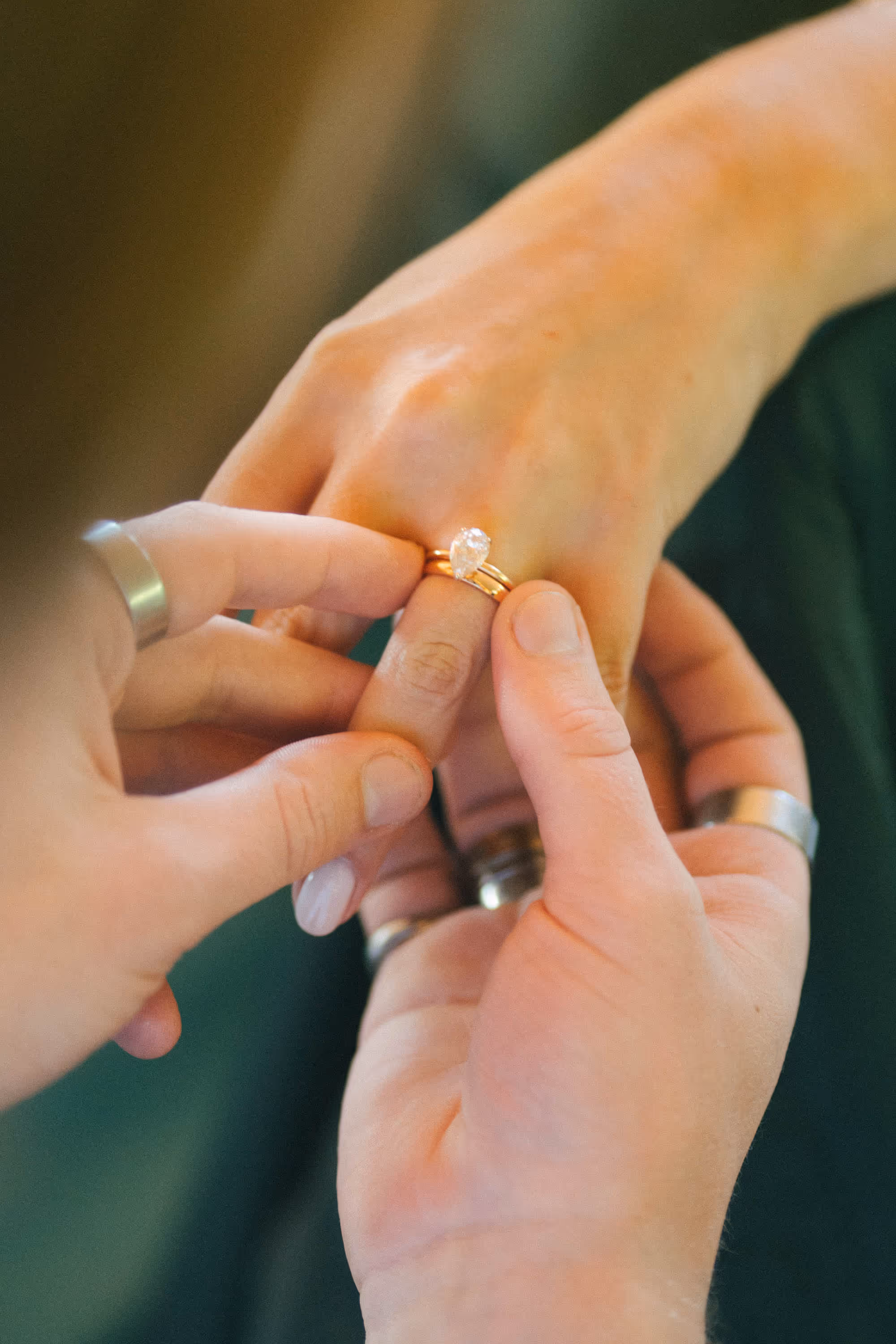 Close-up of a person placing a gold ring with a pear-shaped diamond on another person's finger.