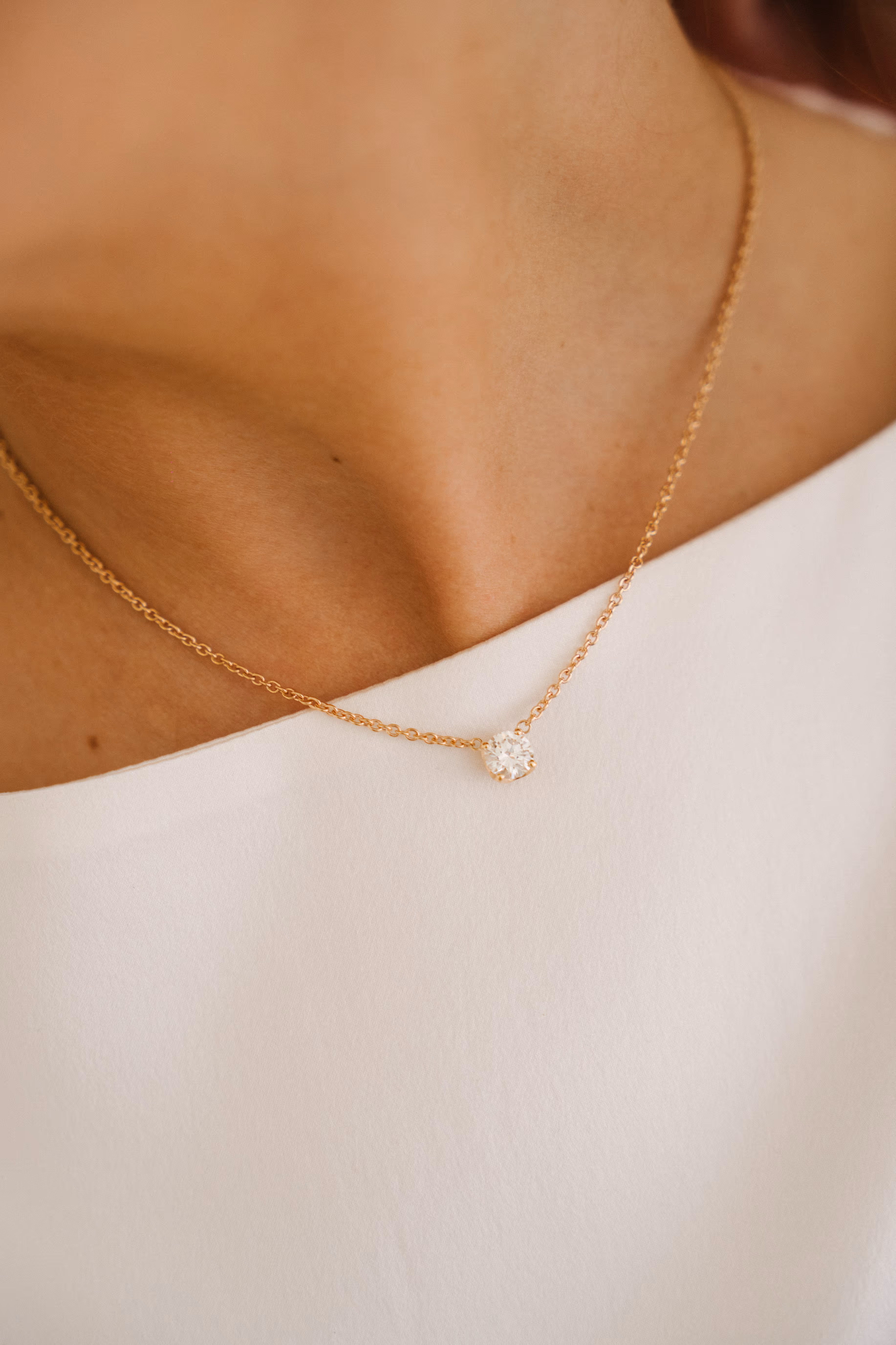 Close-up of a gold chain necklace with a single round diamond pendant worn over a white off-shoulder top.