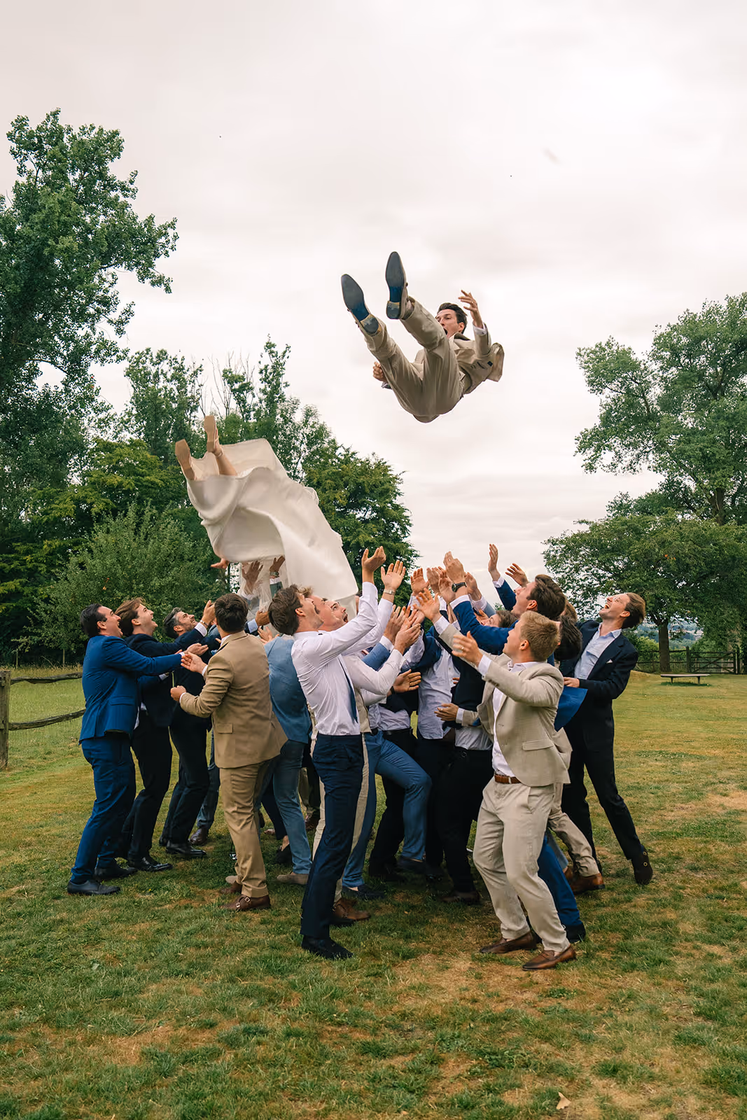 Group of men outdoors tossing a bride and groom into the air during a wedding celebration.